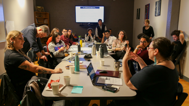 The 2019-2020 reporting fellows around a table at the opening training of the fellowship, all paying attend to one of the fellows speaking from the front of the room 