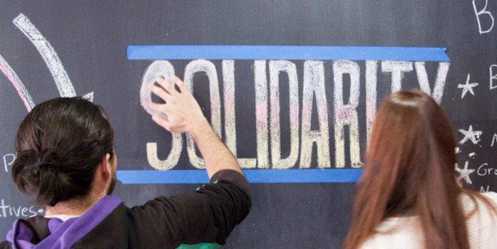 Two people stand in front of a chalkboard reading "Solidarity,"